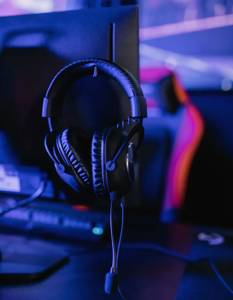Auscultadores profissionais para jogos pendurados num monitor de PC numa estação de jogos moderna com iluminação RGB, prontos para torneios de eSports e jogos multijogador.